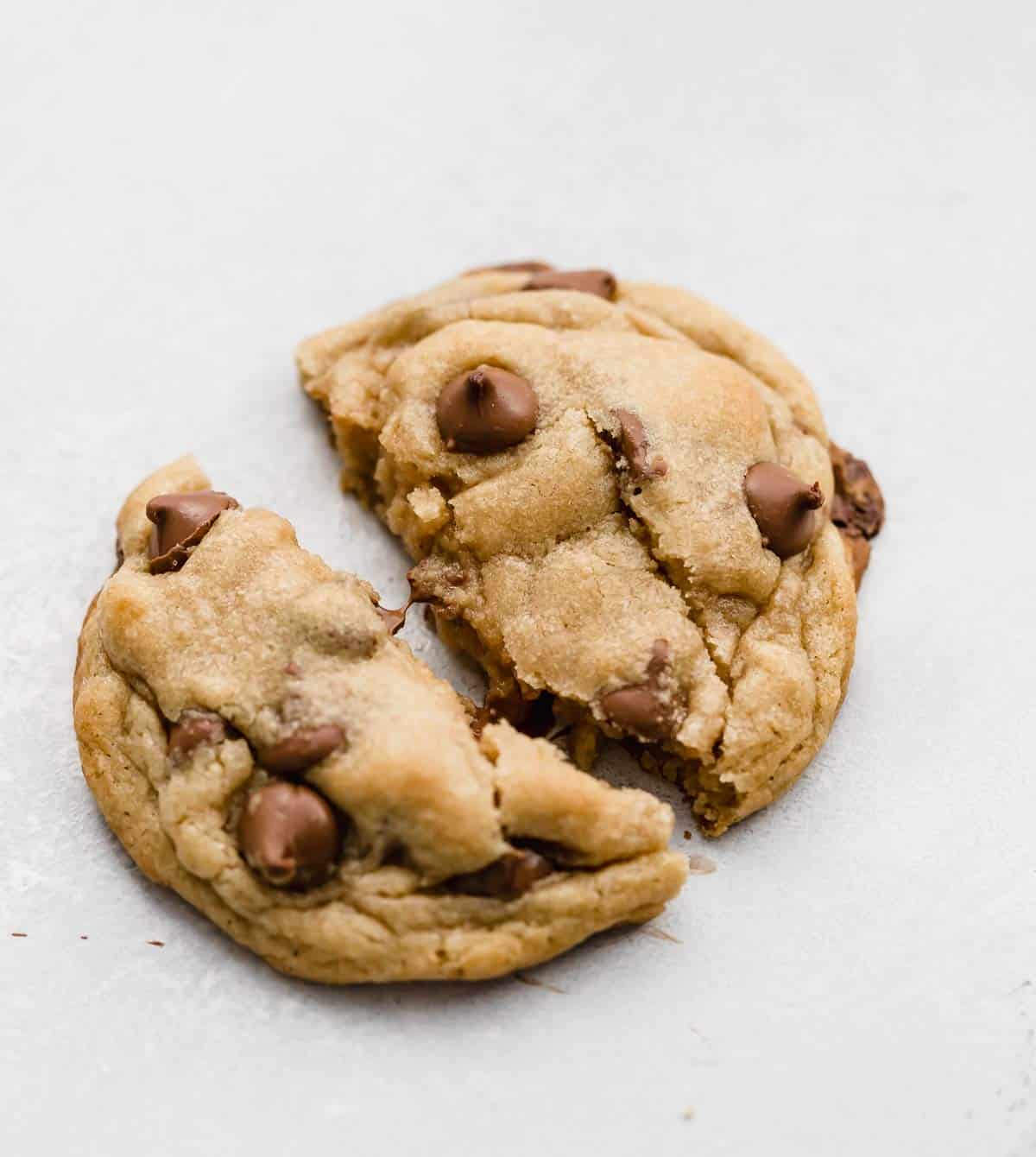 A copycat Crumbl Chocolate Chip Cookie broken in half on a white background.