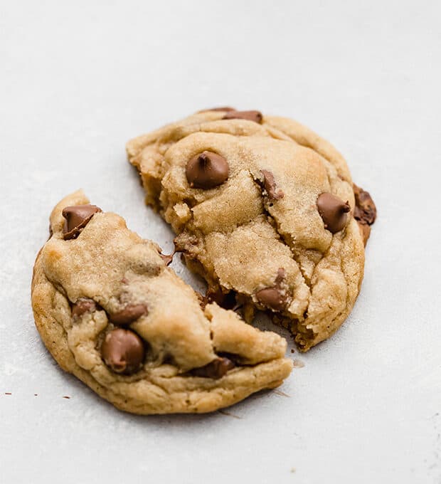 A homemade Crumbl chocolate chip cookie being torn in half.