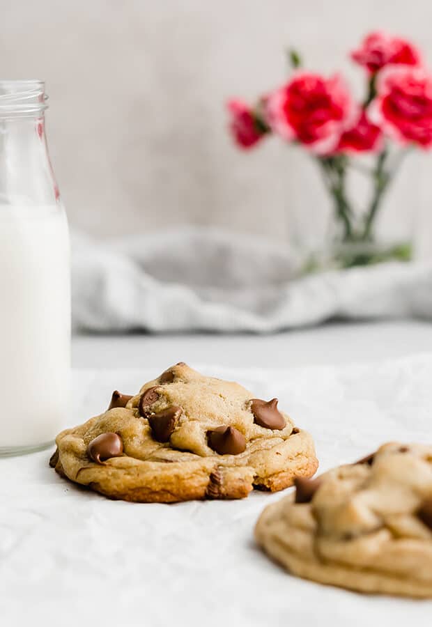 A thick chocolate chip cookie next to a jar of milk.
