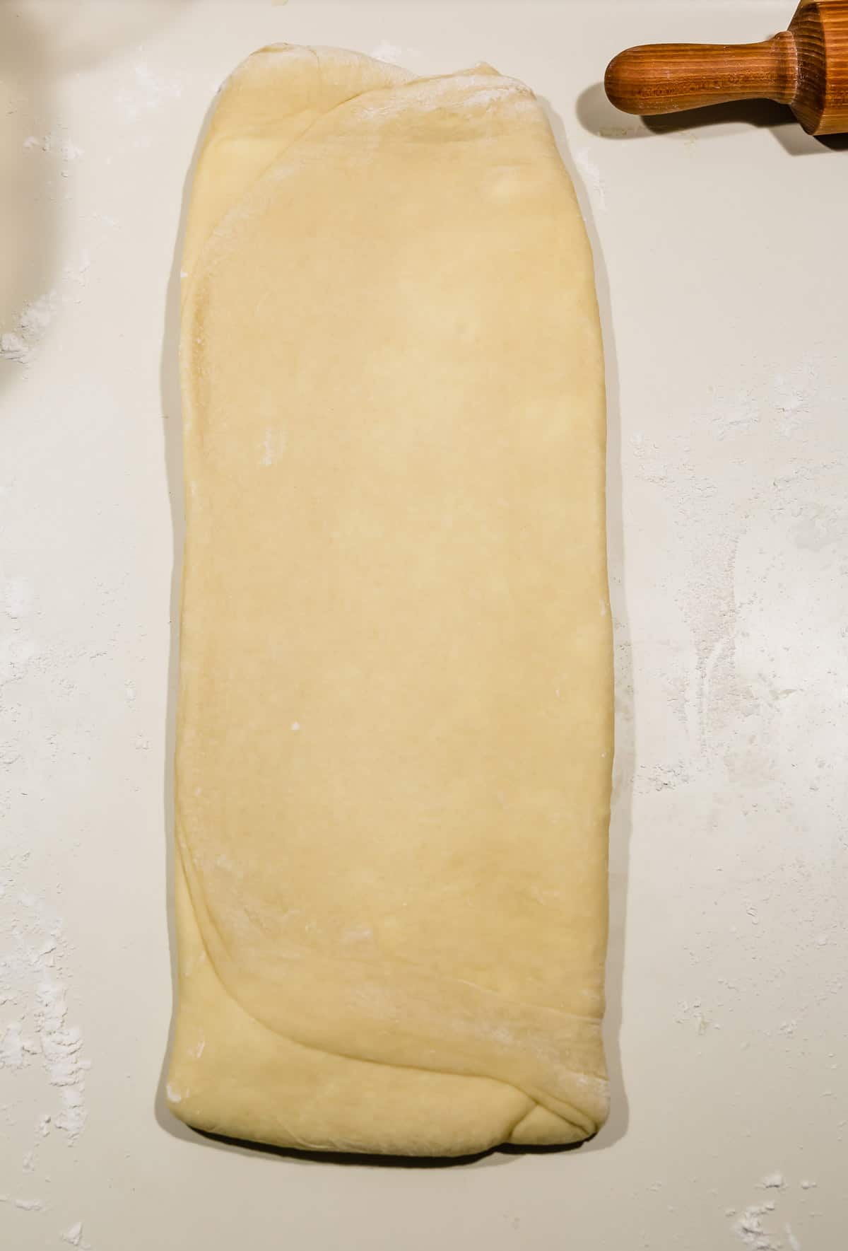 Brioche bread dough rolled out to a long rectangular shape on a white countertop. 