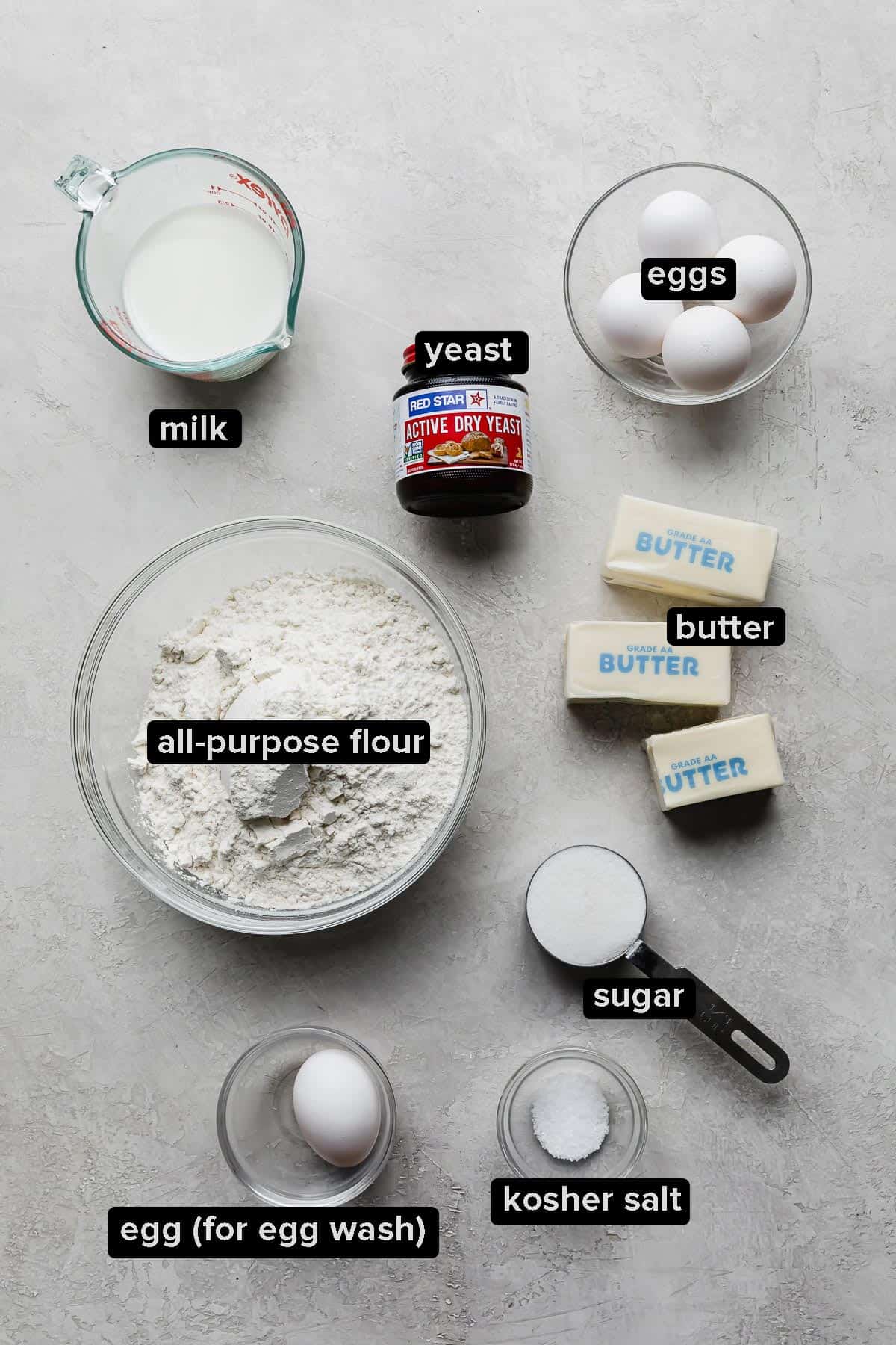 Ingredients used to make flaky brioche bread separated into glass bowls on a gray background.