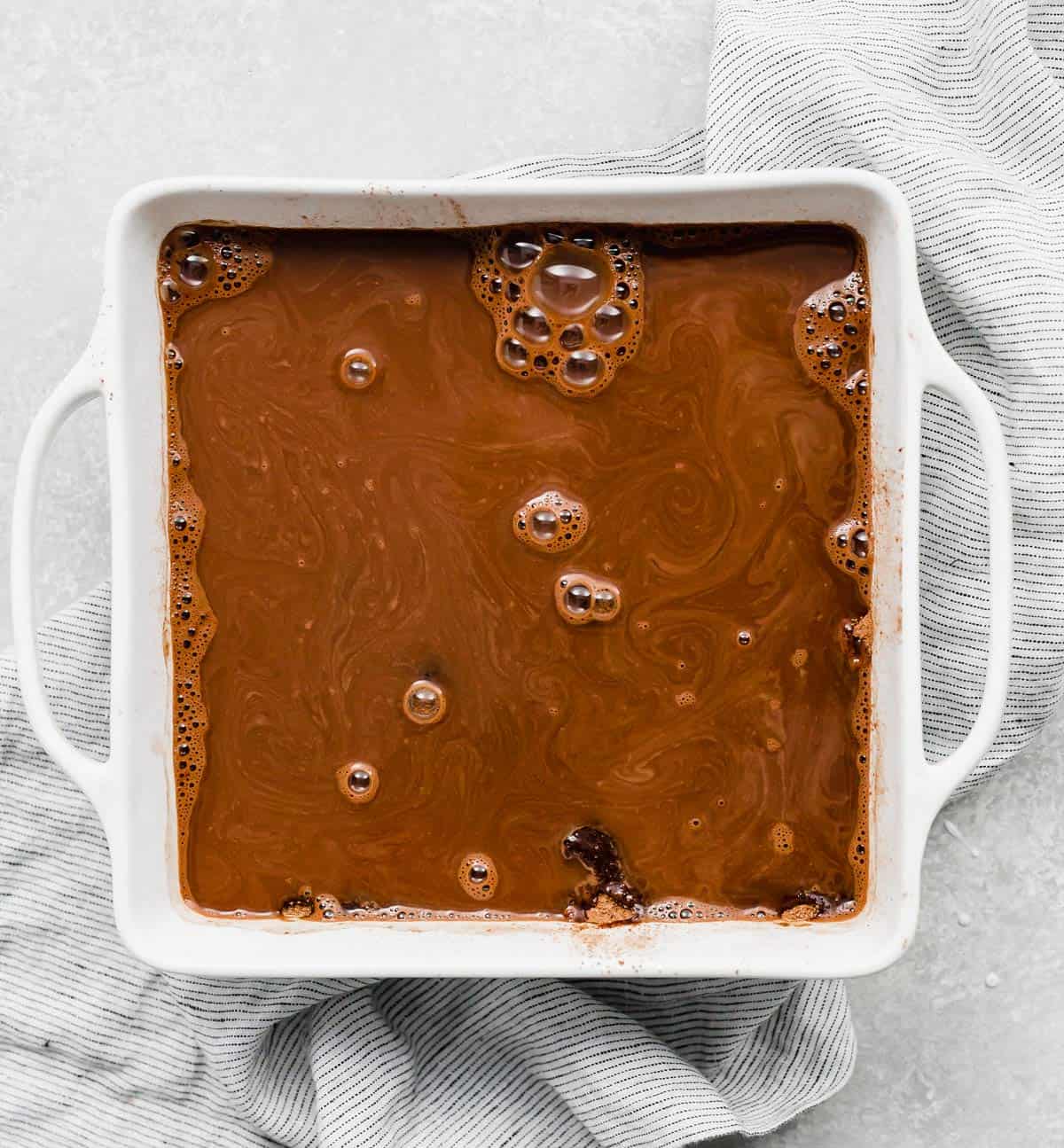 A square white pan with boiling water poured overtop a hot fudge cake batter.