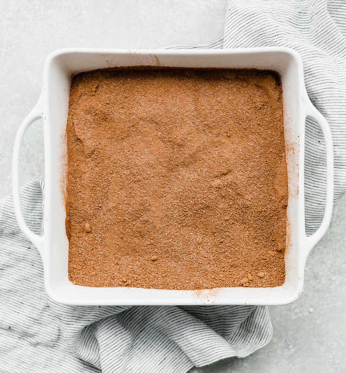 A brown colored sugar mixture overtop a hot fudge cake batter in a white square pan.