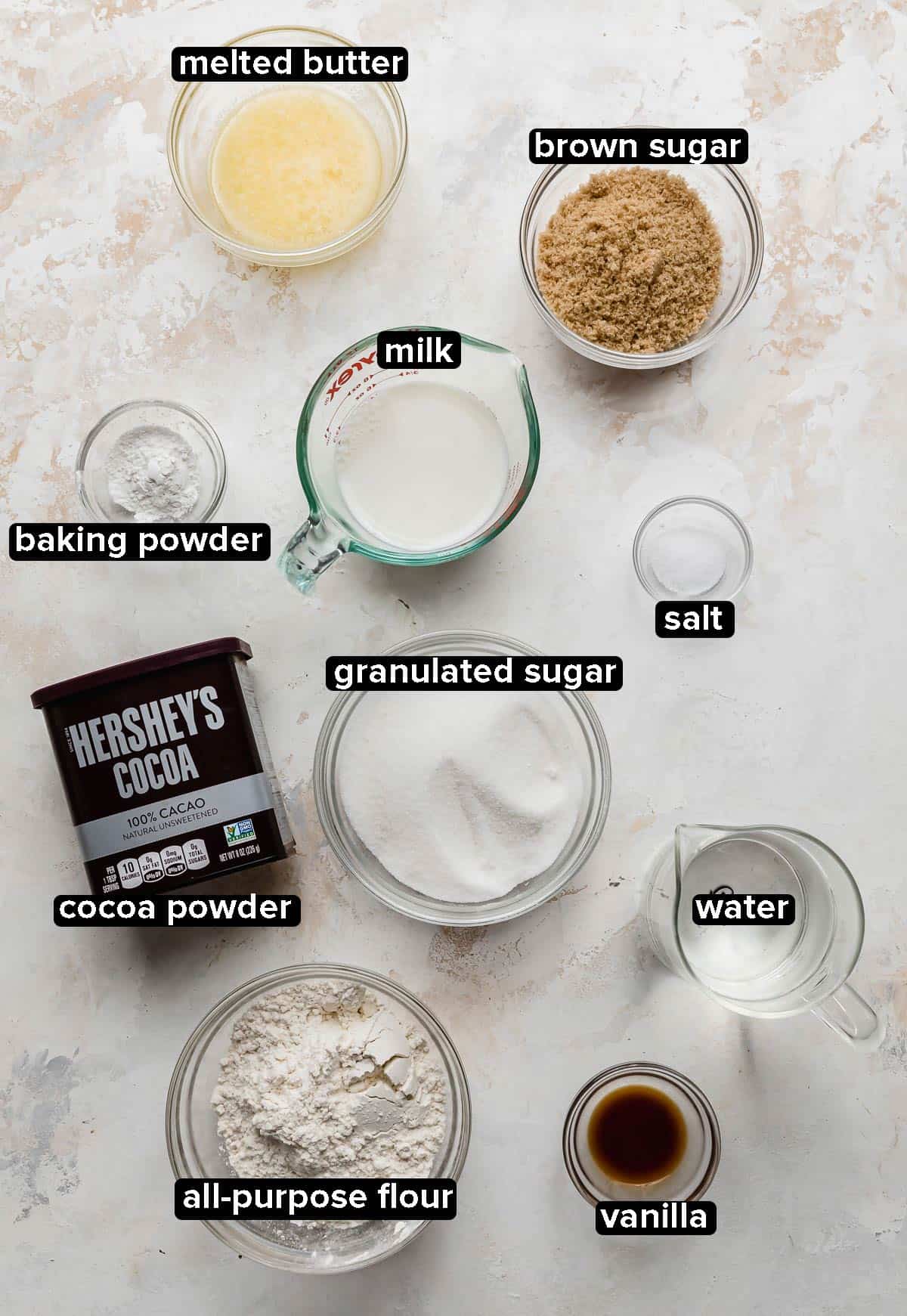 Ingredients used to make Hot Fudge Cake portioned into glass bowls on a white and cream textured background.