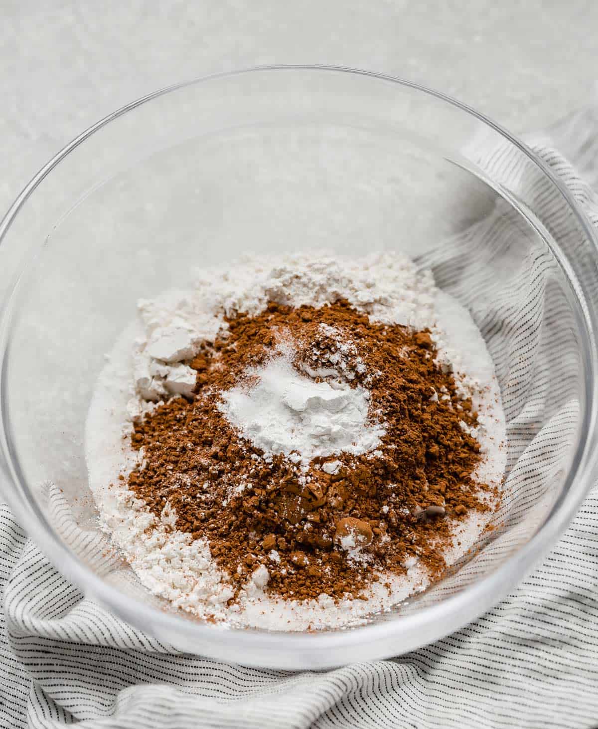 A glass bowl with dry ingredients in it, including baking powder, for making hot fudge pudding cake.