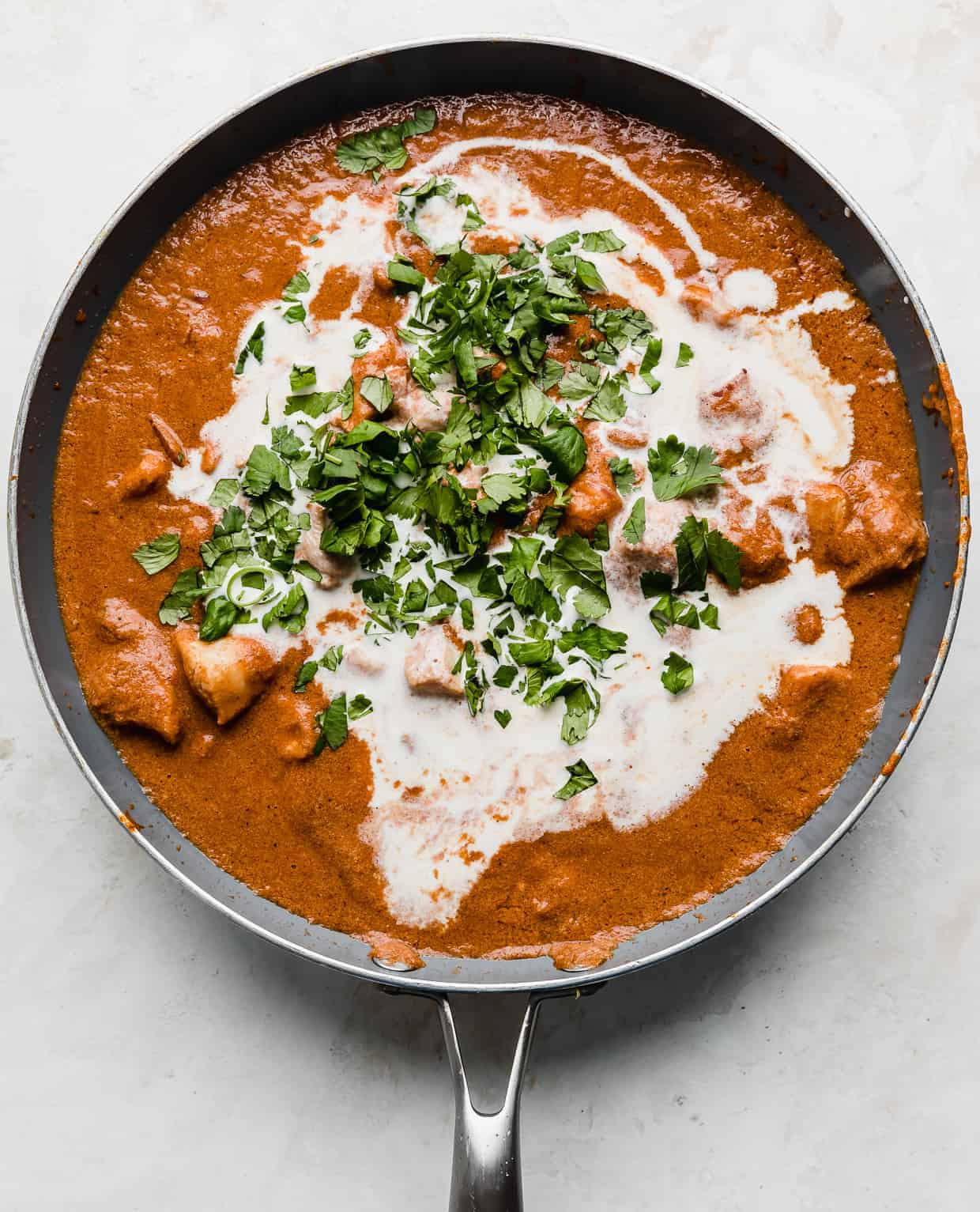 A skillet with Indian Butter Chicken in it with heavy cream and cilantro overtop.