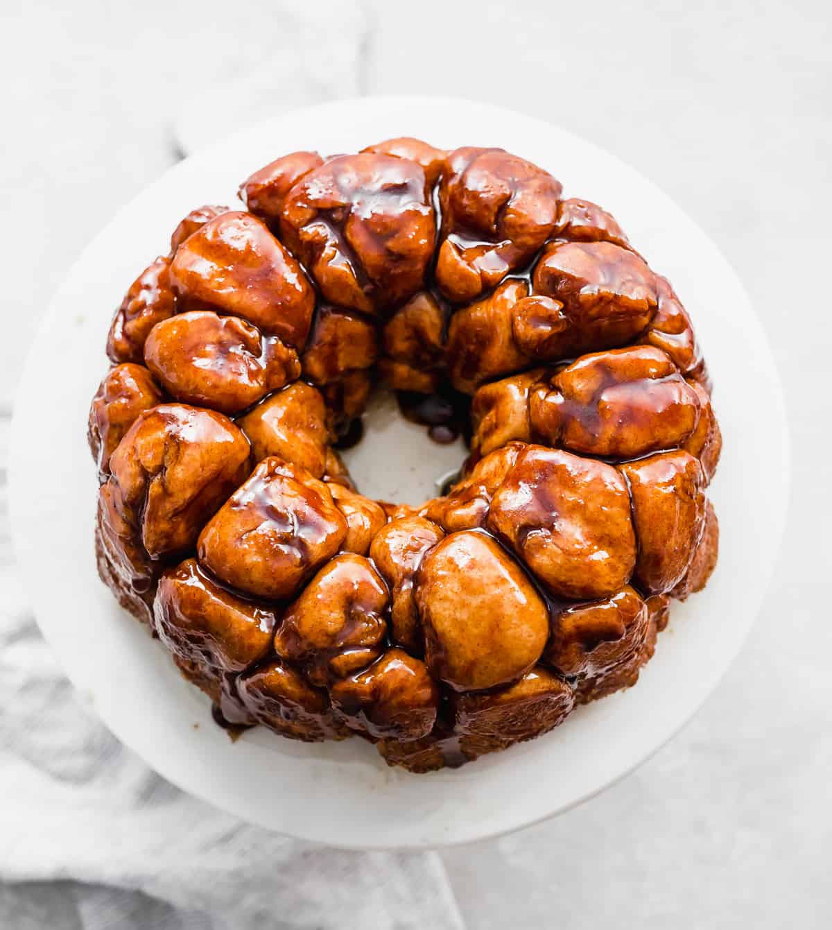 A golden brown baked Monkey Bread recipe made in a bundt pan turned out on a white plate.