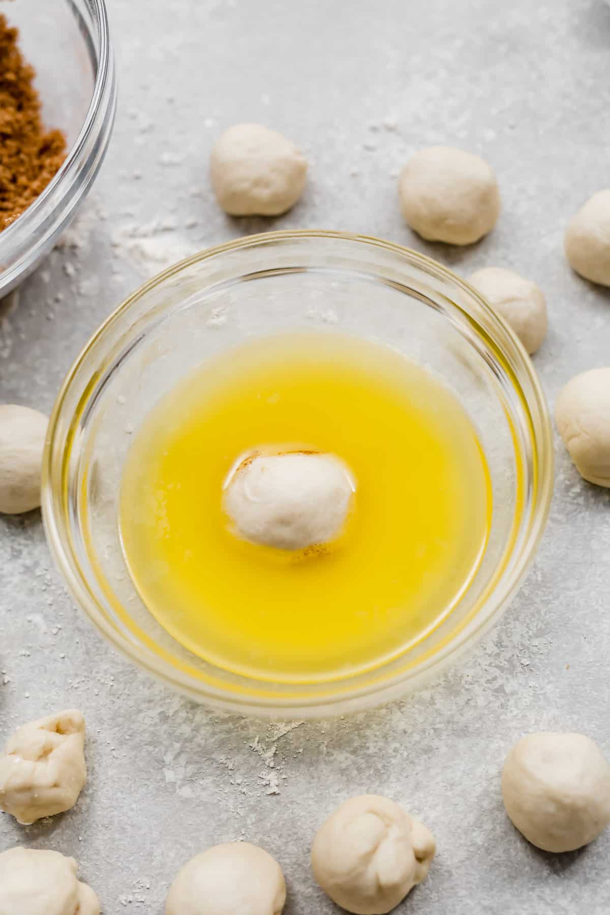 A ball of dough in a glass bowl with melted butter in it.