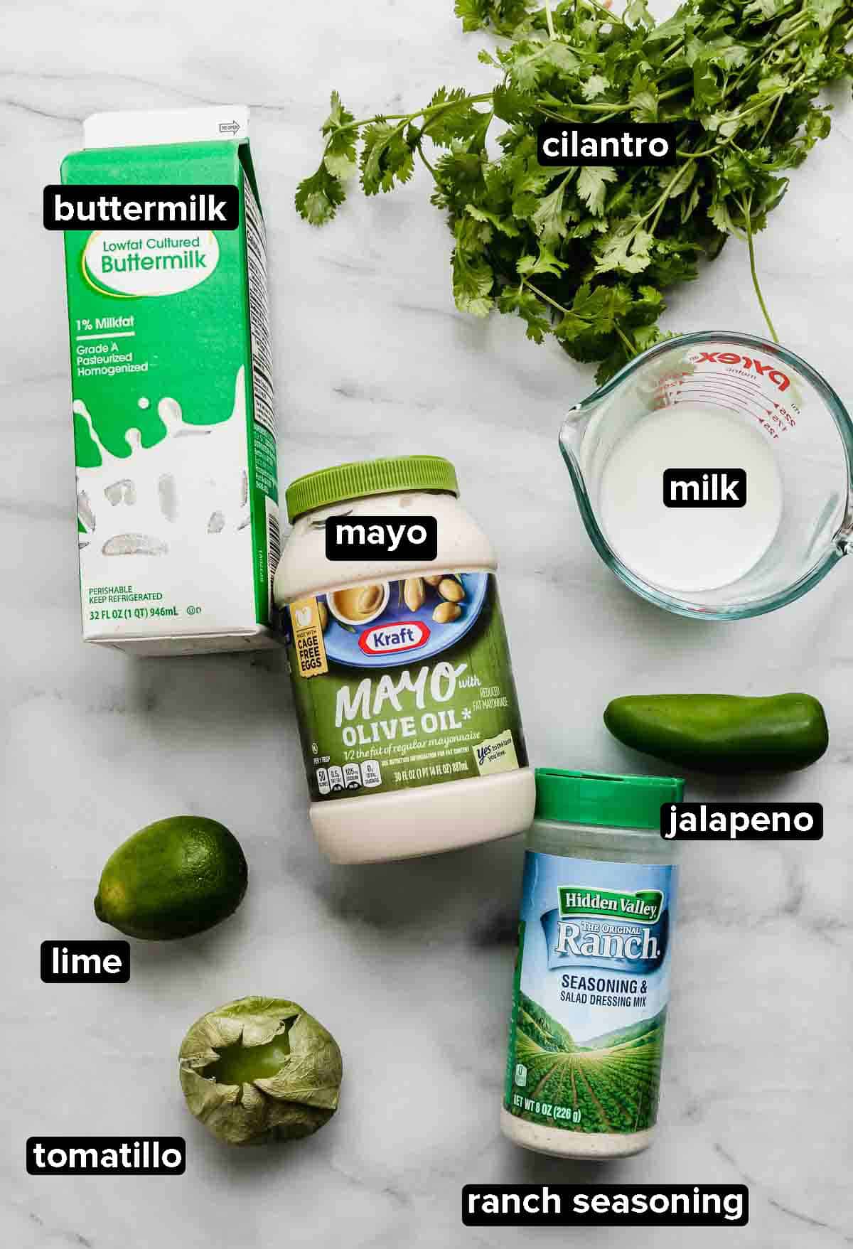 Cilantro Lime dressing ingredients on a white background; ingredients include a tomatillo, jalapeño, buttermilk, cilantro, mayo, ranch seasoning and a lime.