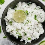A black bowl filled with Cilantro Lime Rice and garnished with a fresh lime slice.