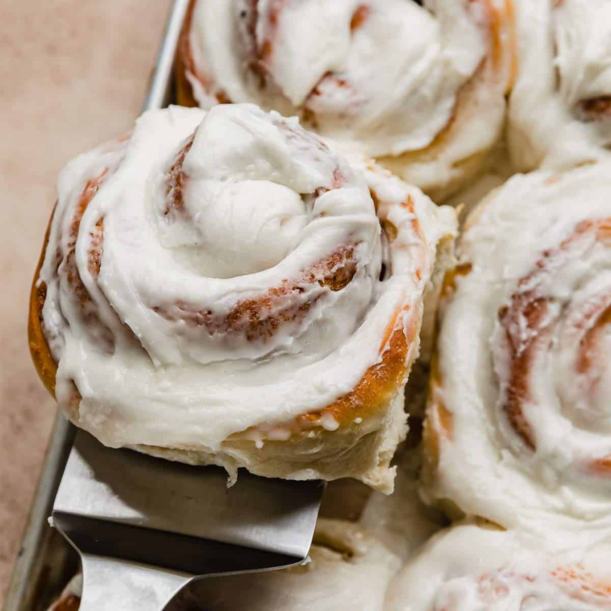 A close up of a vanilla frosting cinnamon roll.
