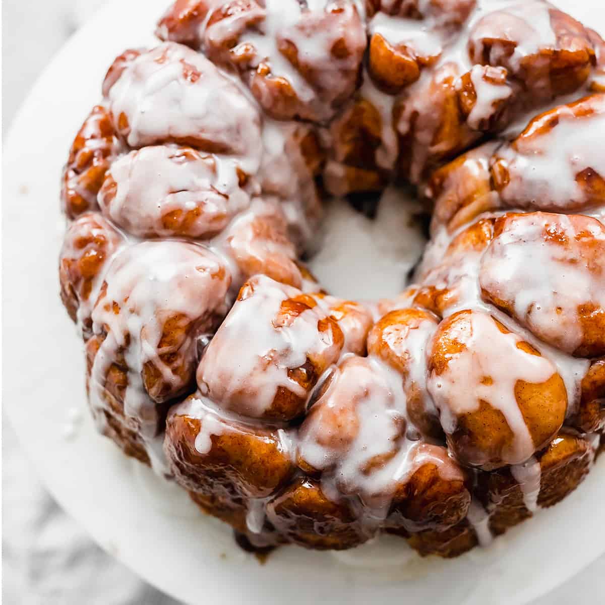 The Best Monkey Bread Recipe covered in a white glaze on a white plate.