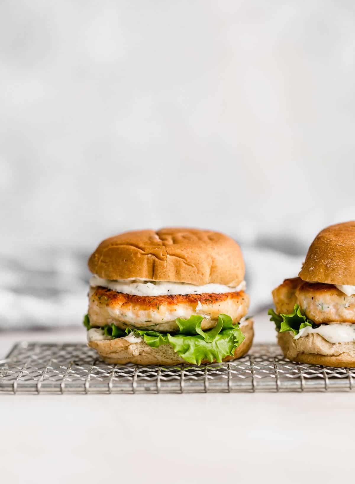 A Salmon Burger on a bun with lettuce and dill sauce.