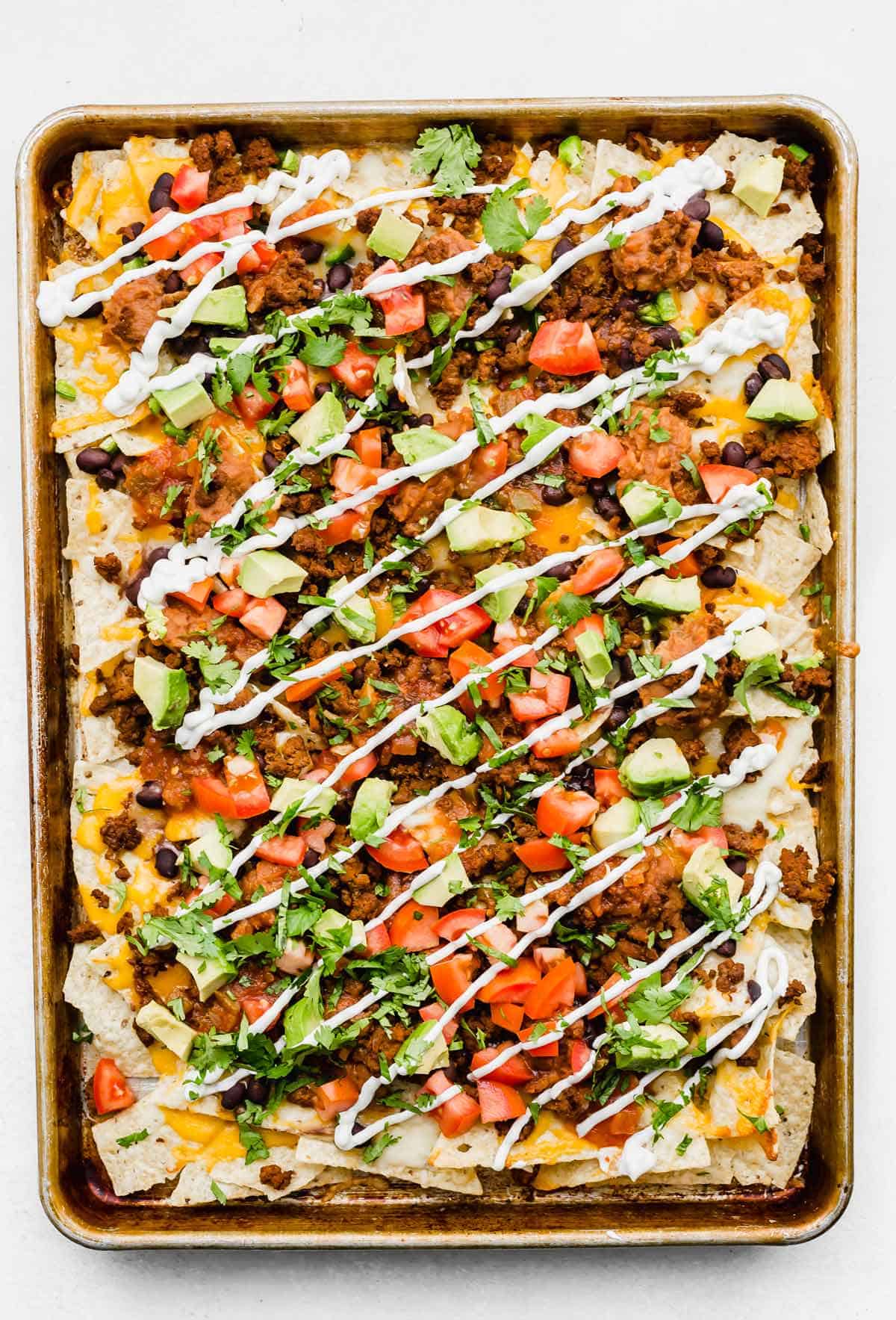 Sheet pan nachos topped with cheese, beef, avocado, cilantro, sour cream, tomatoes.