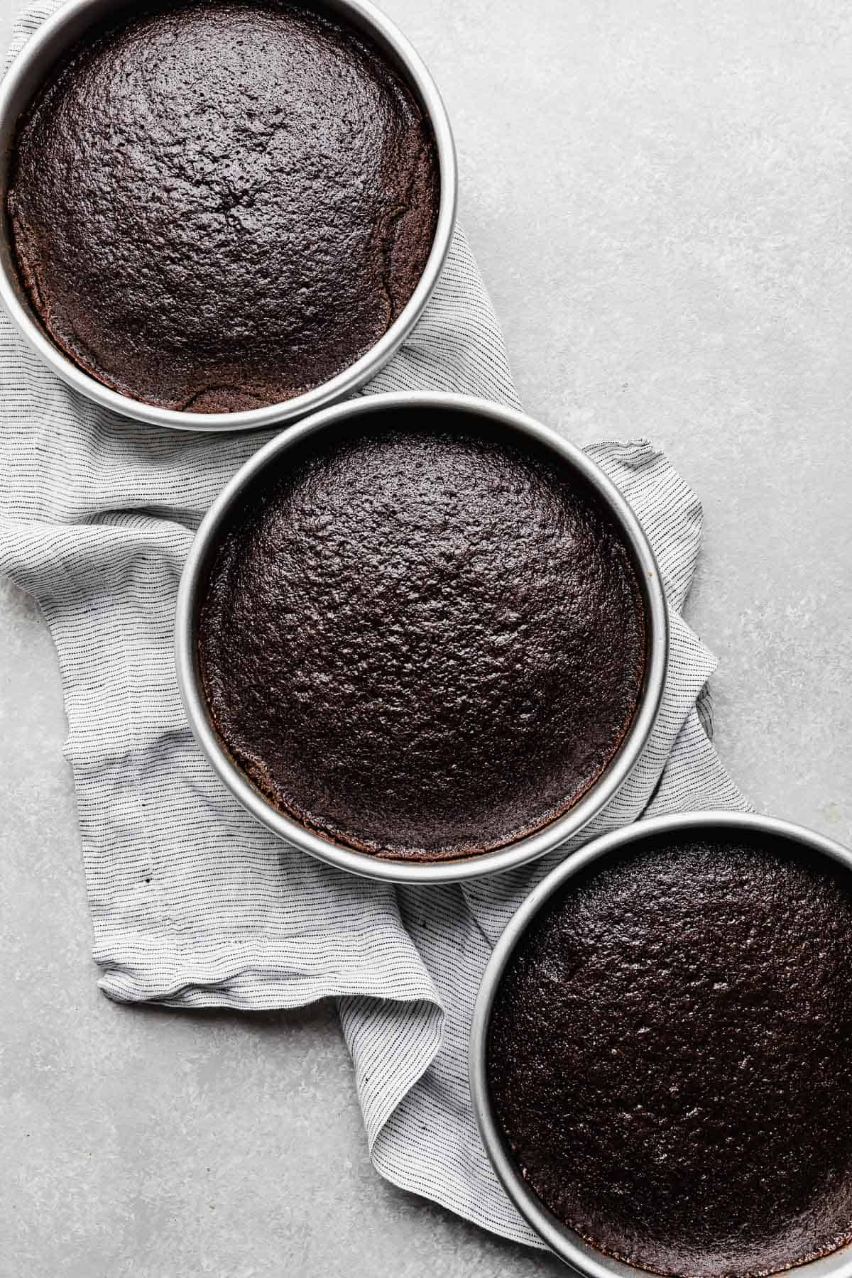Three round cake pans with baked chocolate cake rounds in each pan.