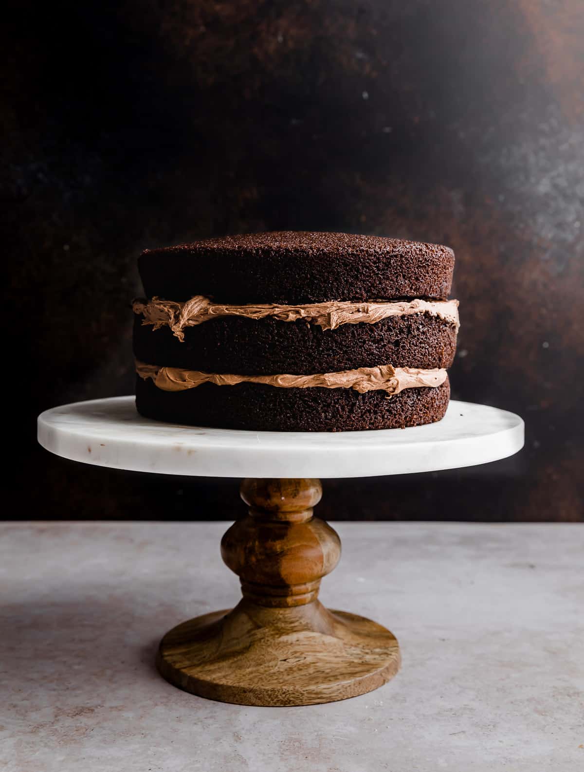 A three tiered chocolate cake with chocolate buttercream frosted between each layer.