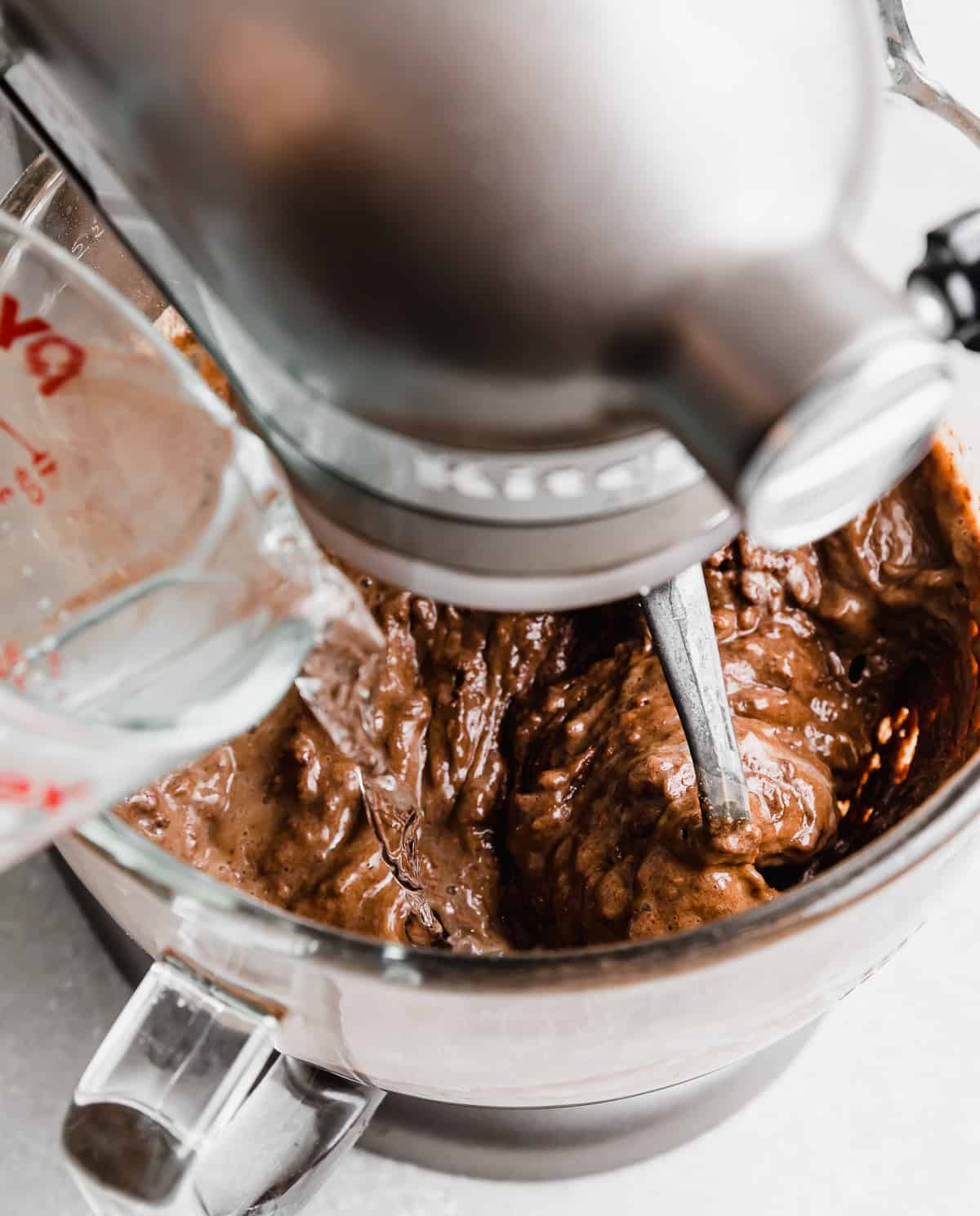 Hot water being poured into a stand mixer bowl that's stirring chocolate cake batter.