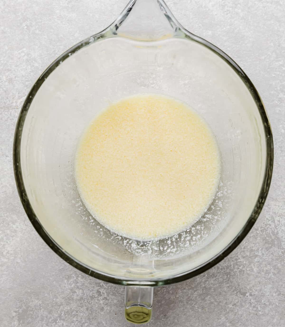 A light yellow colored liquid in a glass stand mixer bowl on a gray background.