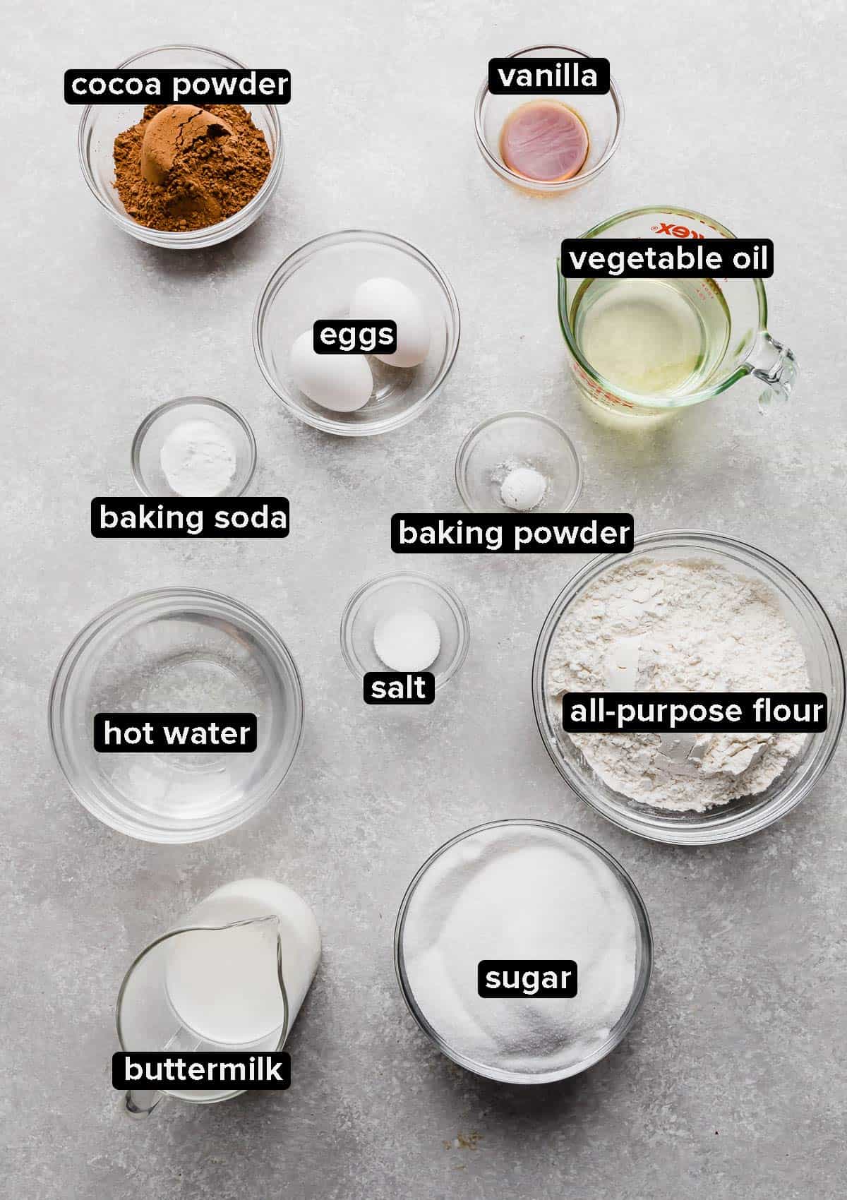 Ingredients used to make a chocolate cake portioned into glass bowls on a white background.