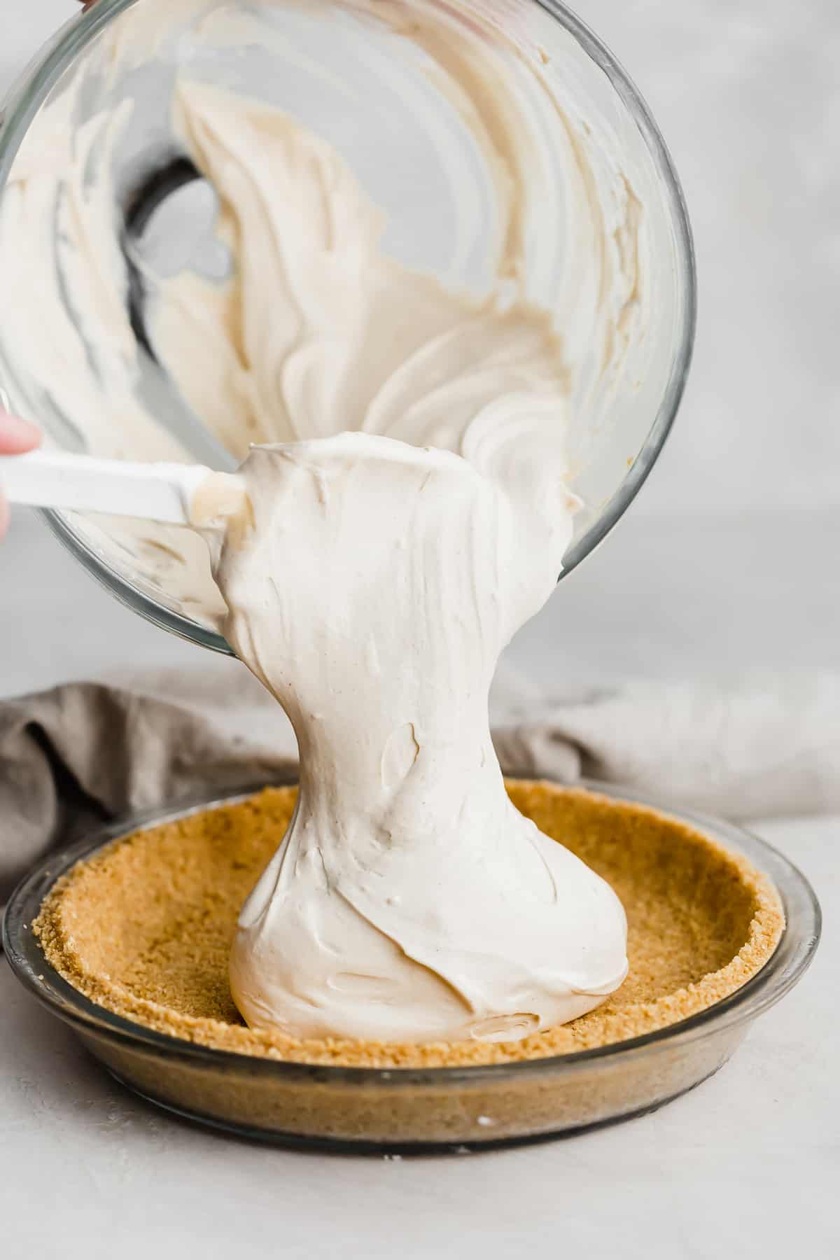 A light tan colored peanut butter mixture being poured into a graham cracker crust.