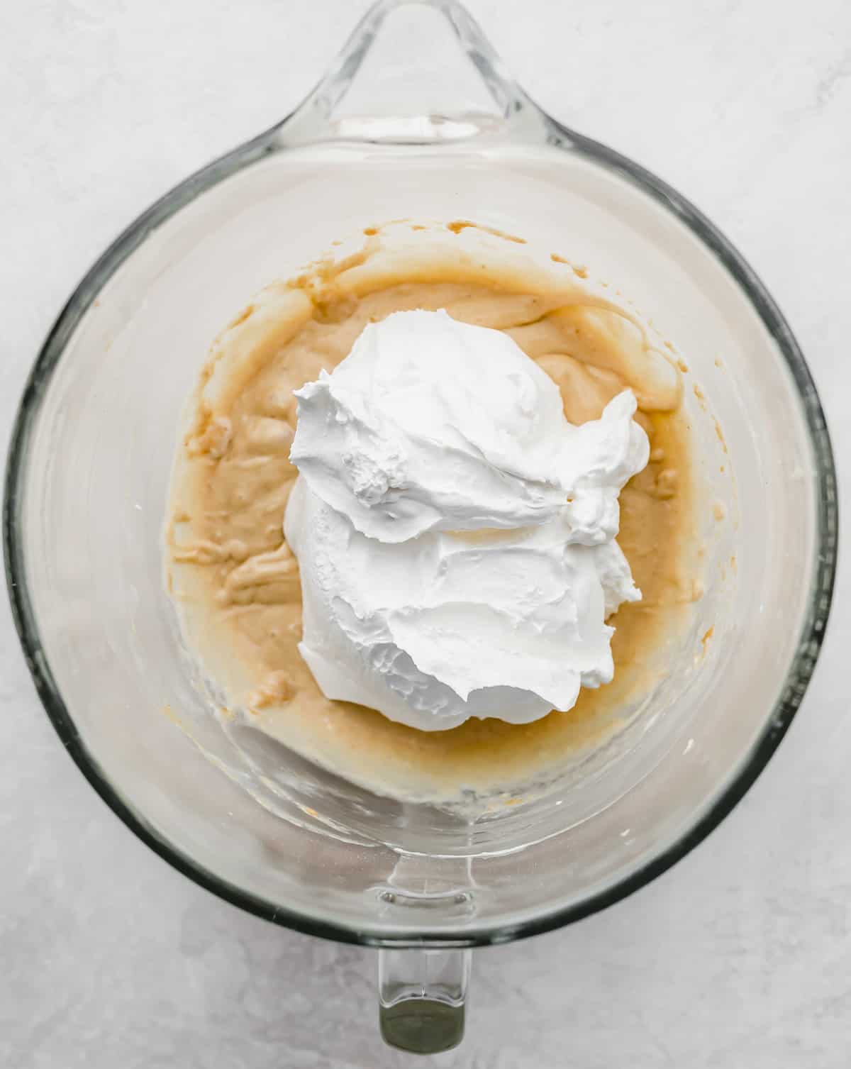 Cool whip on top of a peanut butter mixture in a glass bowl.