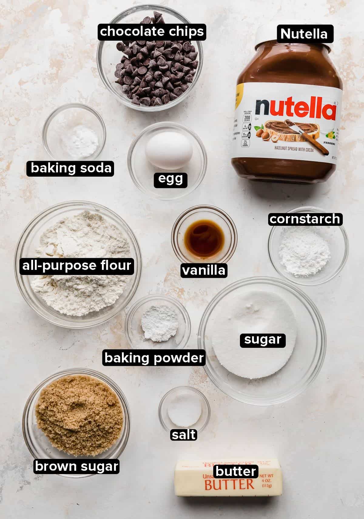 Ingredients used to make Nutella Stuffed Nutella Cookies portioned into glass bowls on a white background.