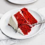 A slice of the best layered red velvet cake topped with white frosting on a white plate.