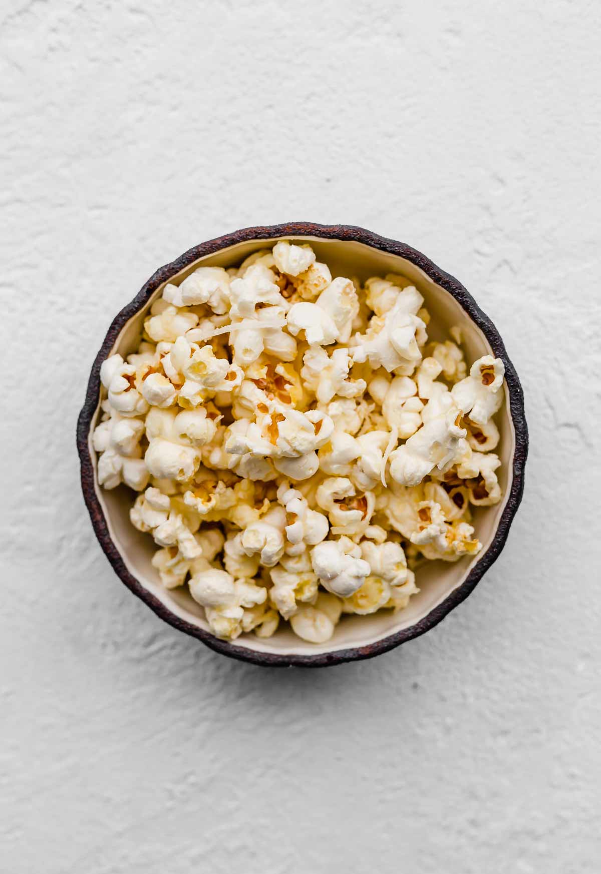 Parmesan Popcorn in a black bowl on a white textured background.