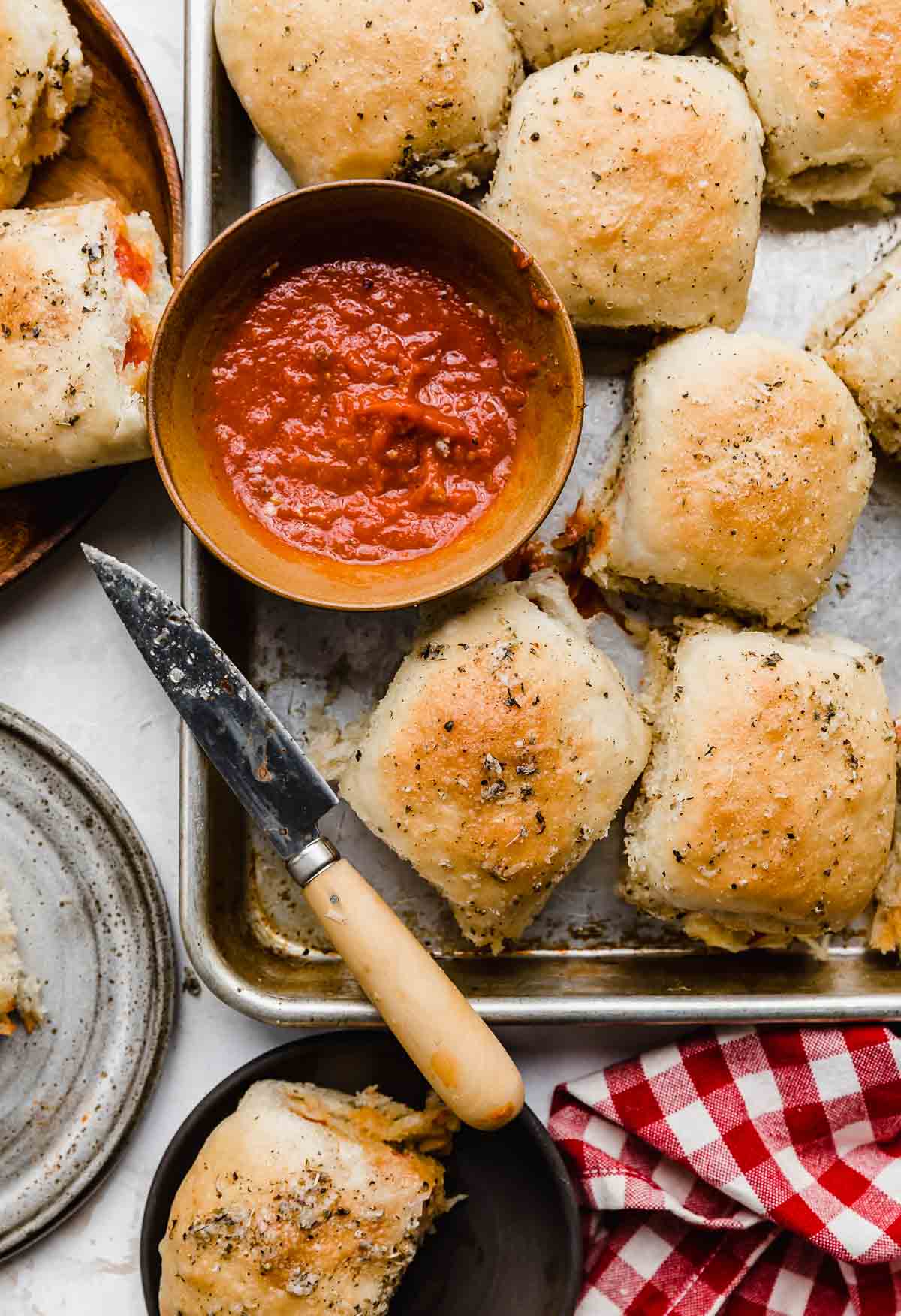 Overhead photo of a baking sheet topped with pizza rolls and a bowl of red dipping sauce.