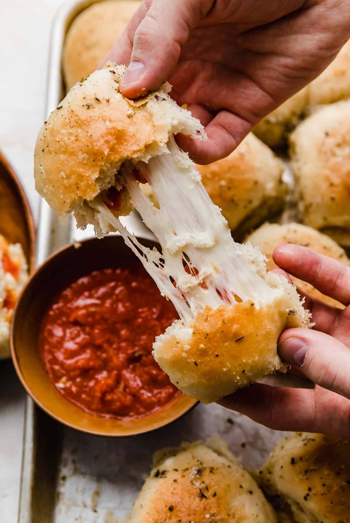 Two hands pulling a pizza roll apart showing the inside stretchy mozzarella cheese.