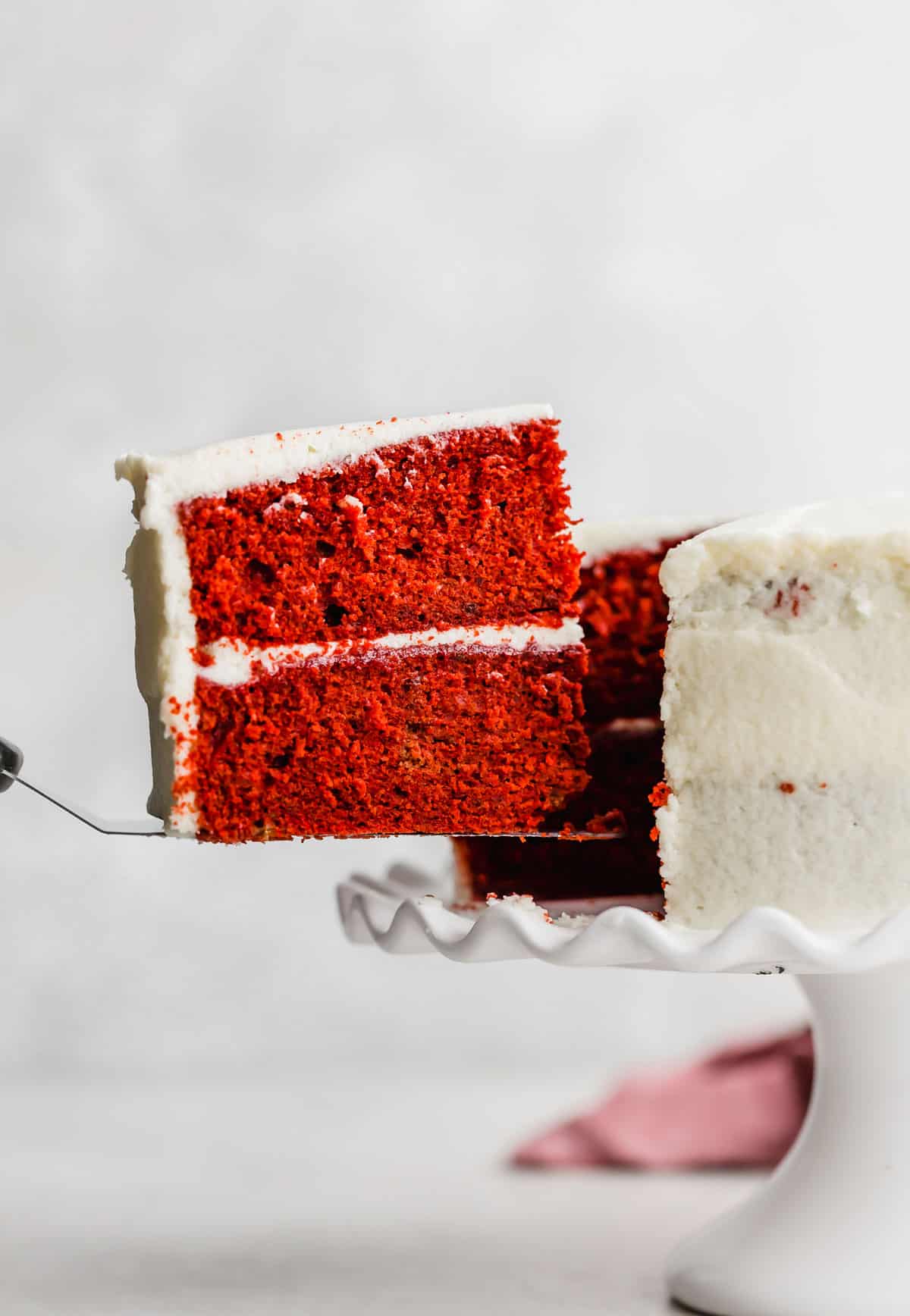 A slice of Old Fashioned Red Velvet Cake being lifted out of a white frosted cake.