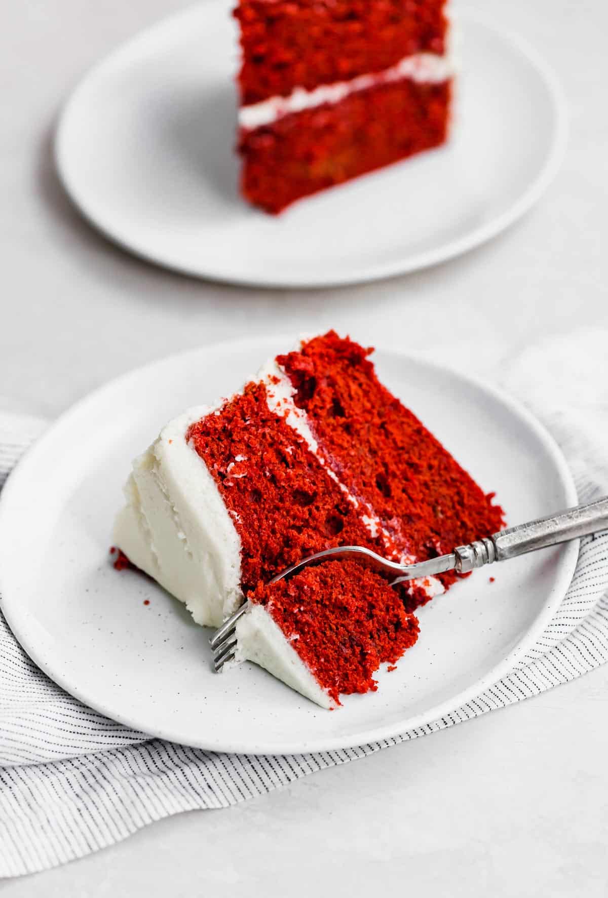 A slice of Old Fashioned Red Velvet Cake topped with old fashioned frosting on a white plate.