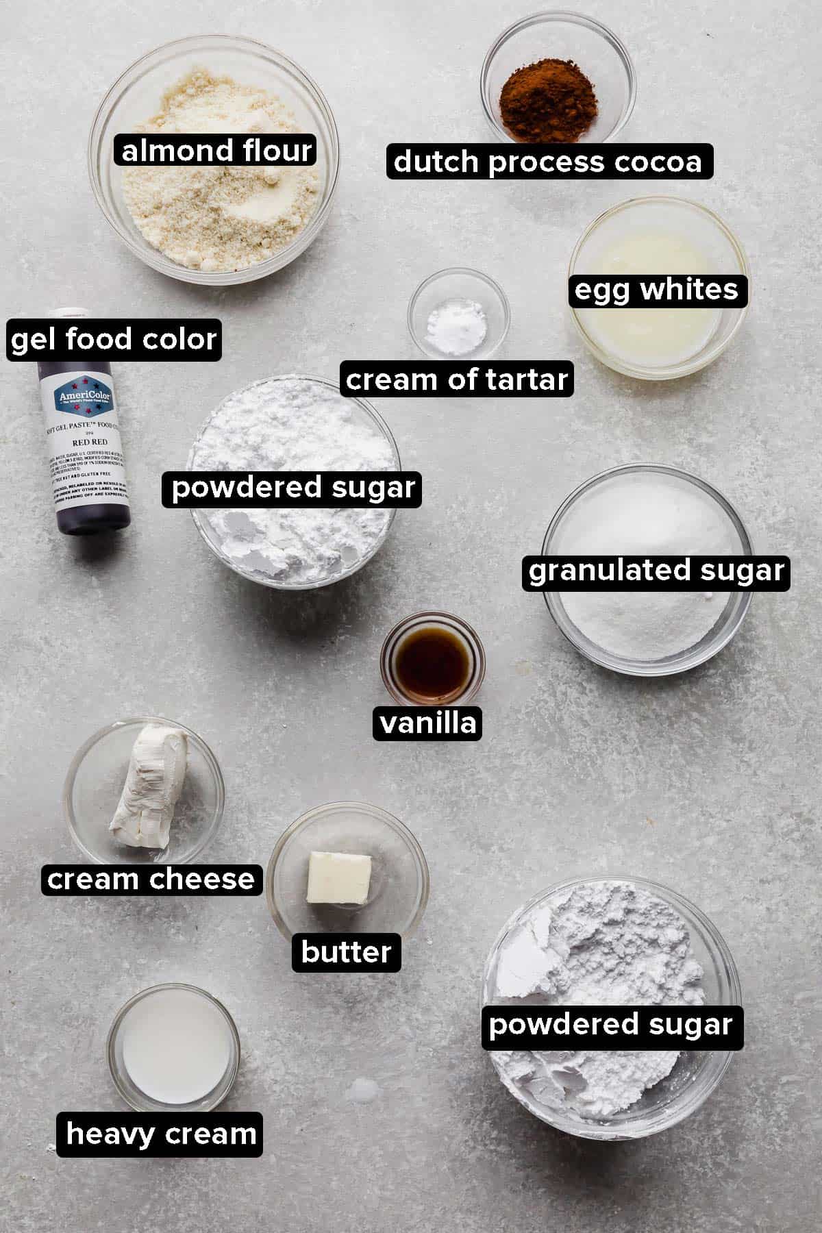 Ingredients used to make Red Velvet Macarons, each ingredient portioned into glass bowls on a gray background.