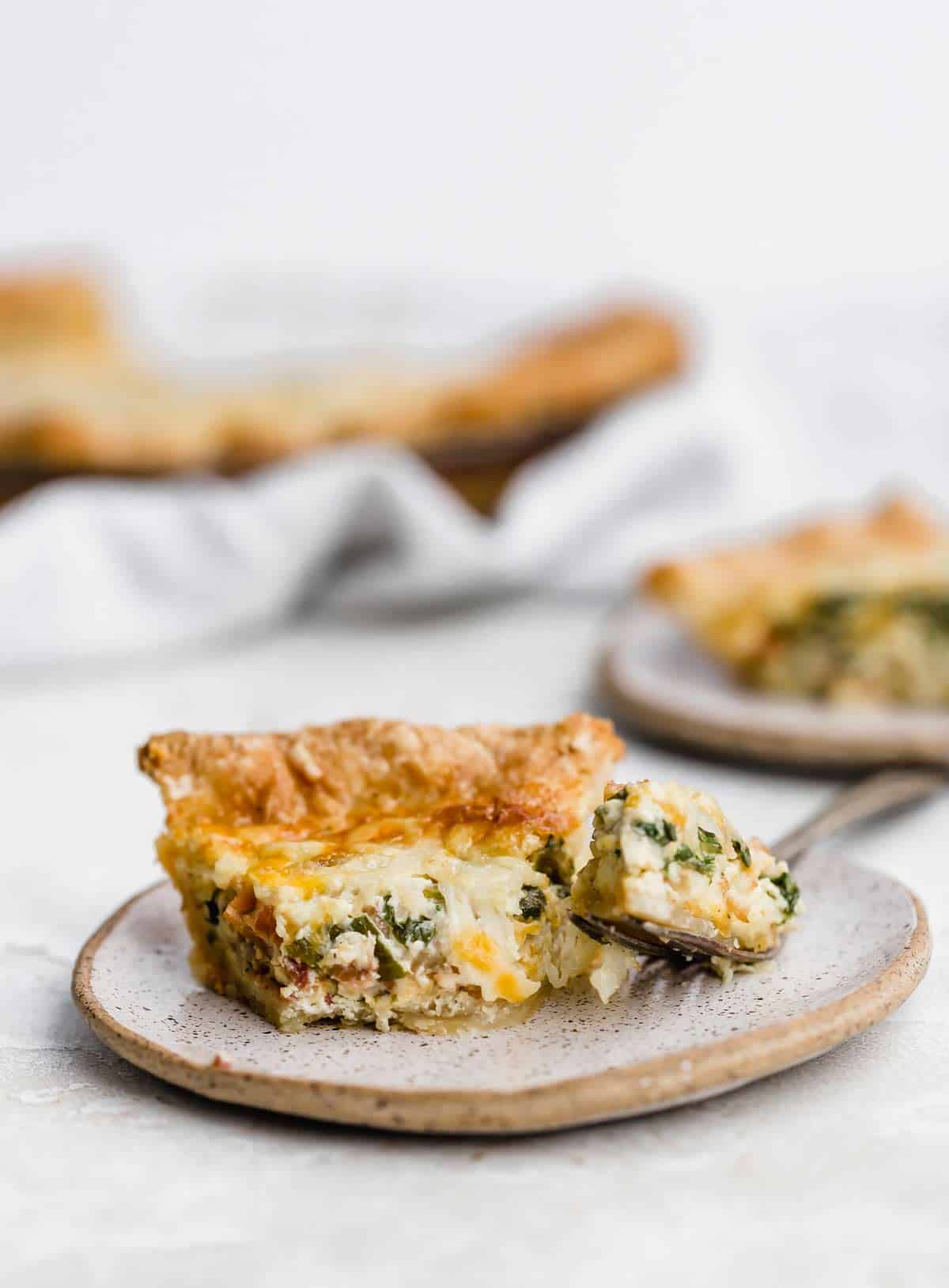 Spinach and Bacon Quiche on a beige plate with a fork next to the pie slice.