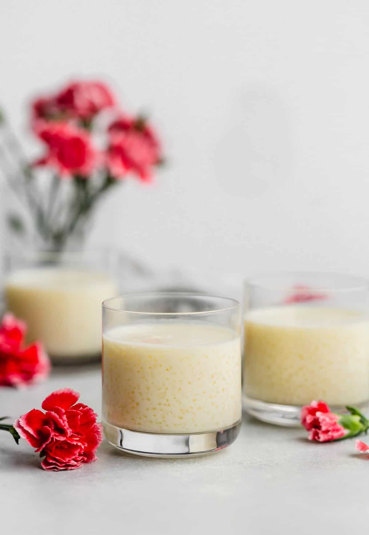 Tapioca Pudding in three glass cups with pink flowers in the background.