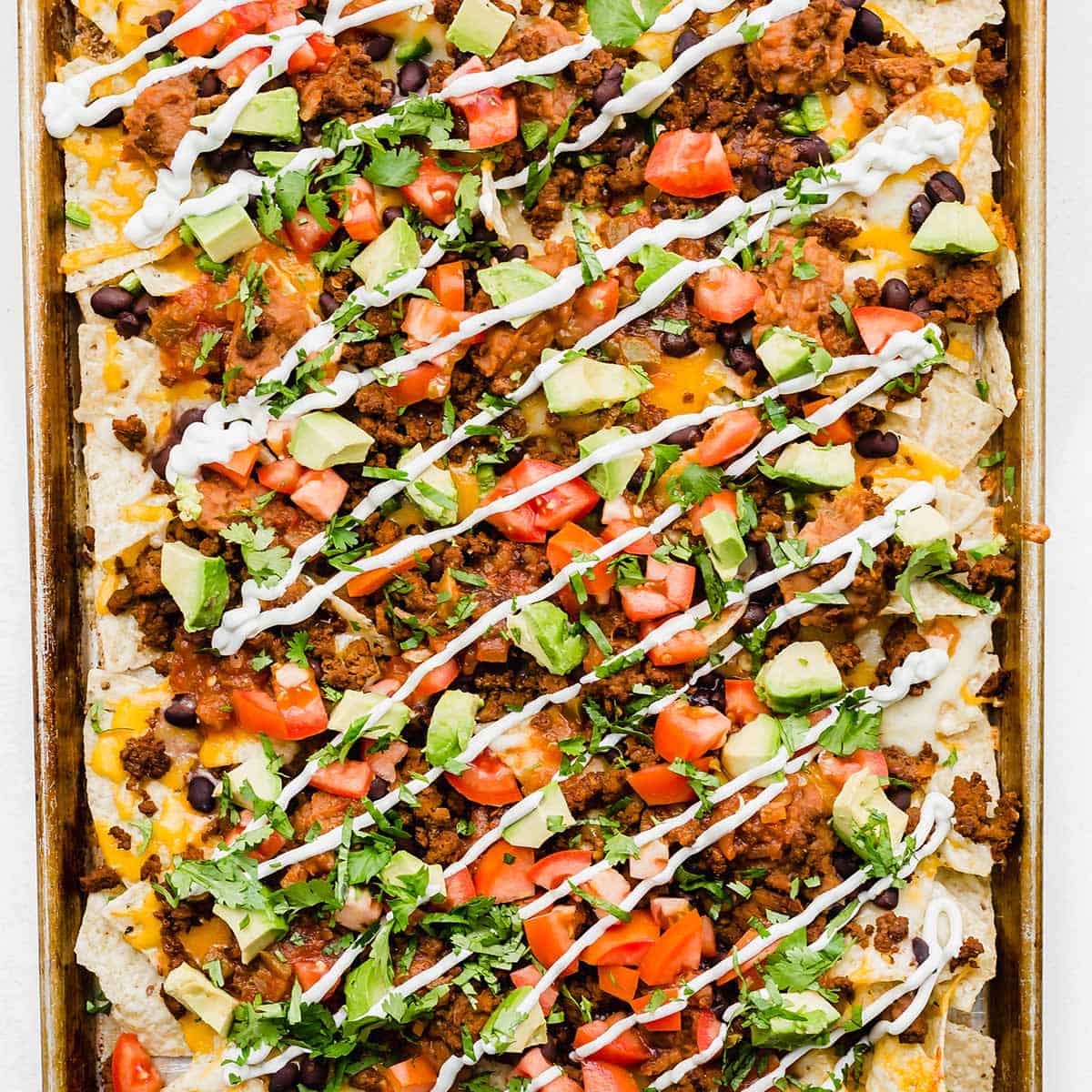 Sheet pan nachos topped with beef, sour cream, tomatoes, cilantro, and avocado.