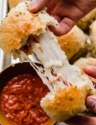 Two hands pulling a pizza roll apart showing the stretchy mozzarella cheese and pepperoni inside.