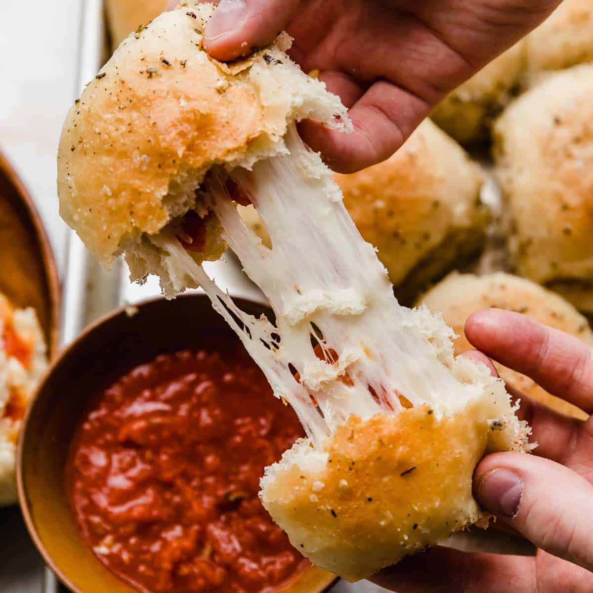 Two hands pulling a pizza roll apart showing the stretchy mozzarella cheese and pepperoni inside.