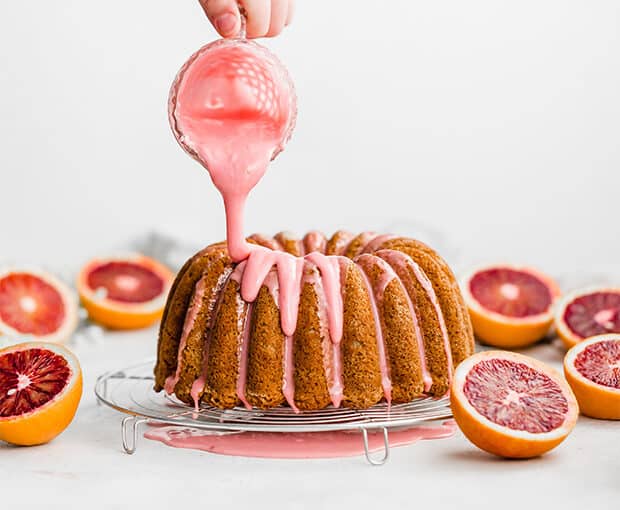 A blood orange glaze being drizzled overtop a blood orange cardamom Bundt Cake.