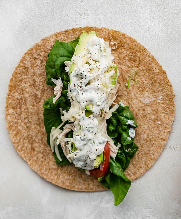 A whole wheat tortilla topped with spinach, shredded chicken, sliced tomatoes, avocado, and shredded cheese.