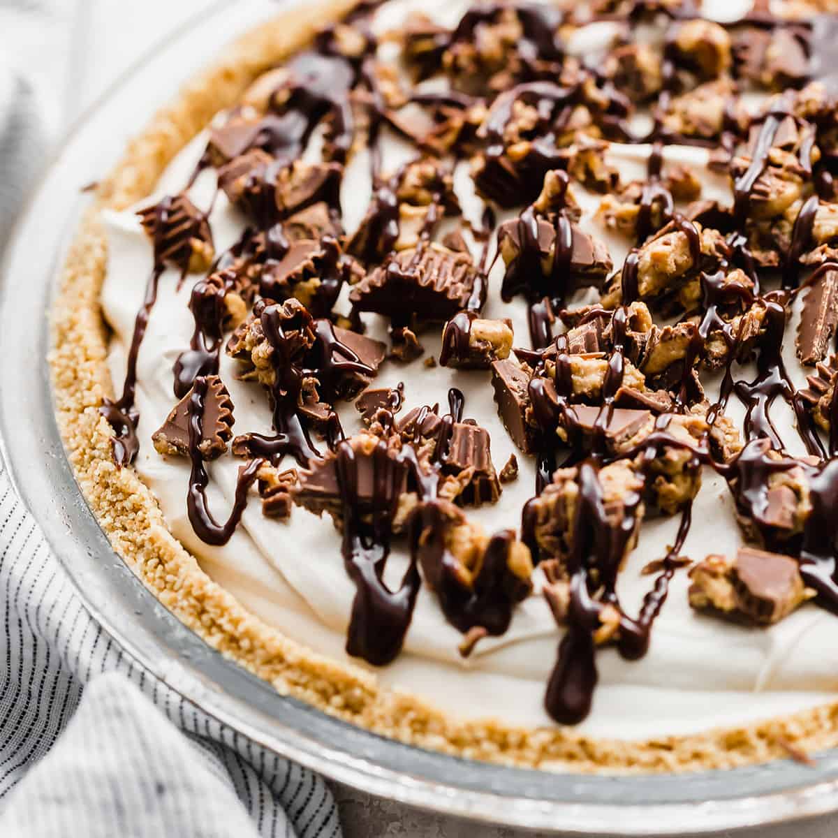 A No-Bake Peanut Butter Pie topped with hot fudge and chopped peanut butter cups.