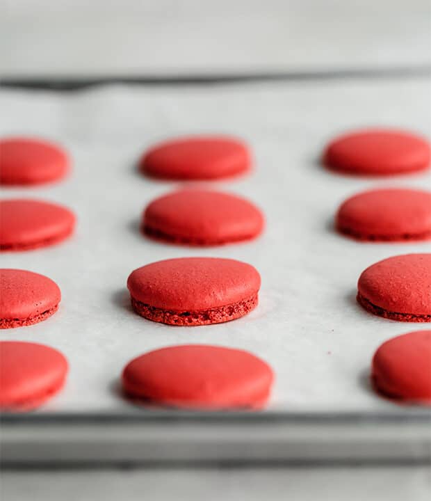 Une plaque à pâtisserie de macarons de Velours Rouge fraîchement cuits au four.