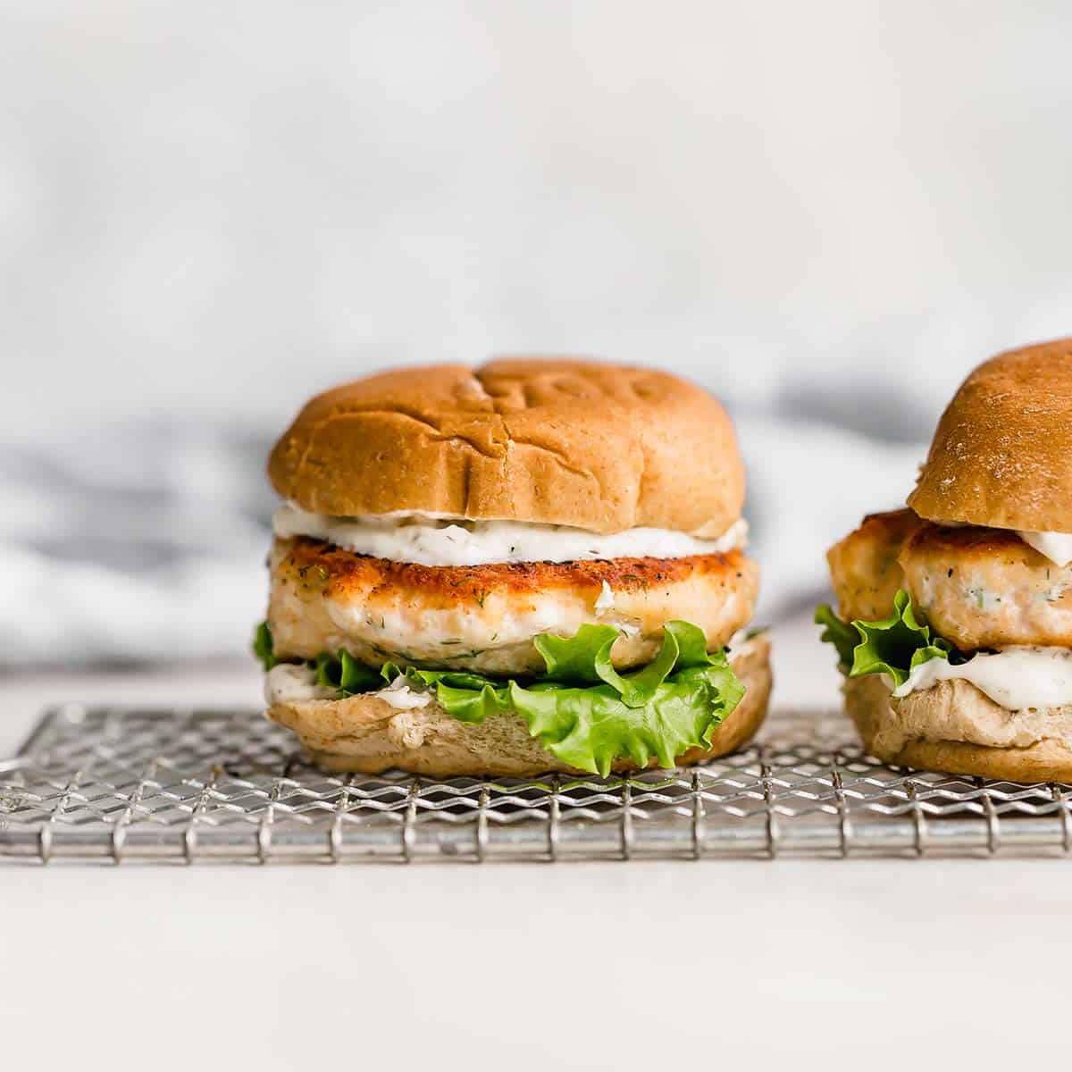 Salmon Burgers with dill sauce on a bun against a white background.