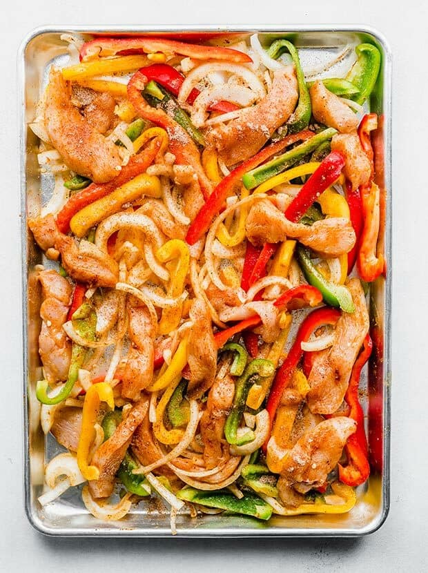 A baking sheet with sliced chicken, peppers, and onions on it.