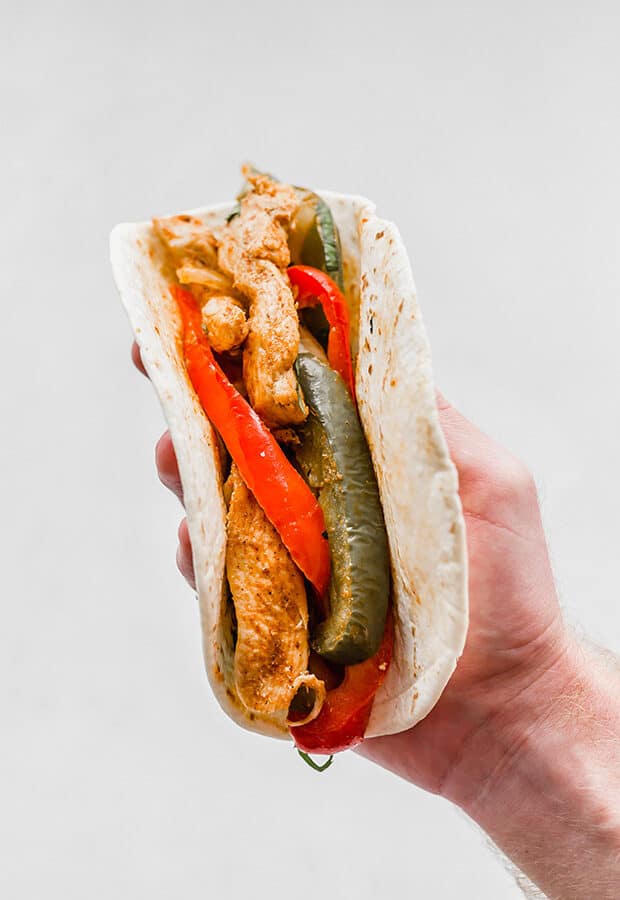 A hand holding a flour tortilla loaded chicken fajita.