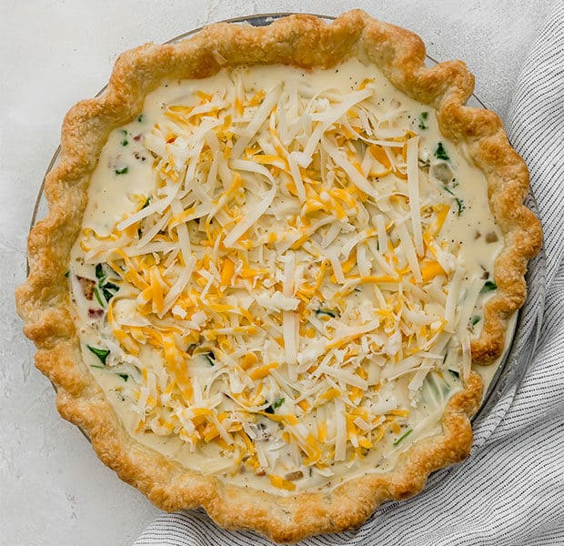 A par baked pie crust with spinach and bacon quiche filling.