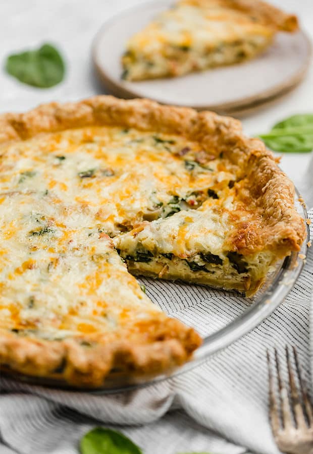 A slice of spinach and bacon quiche in a pie plate.