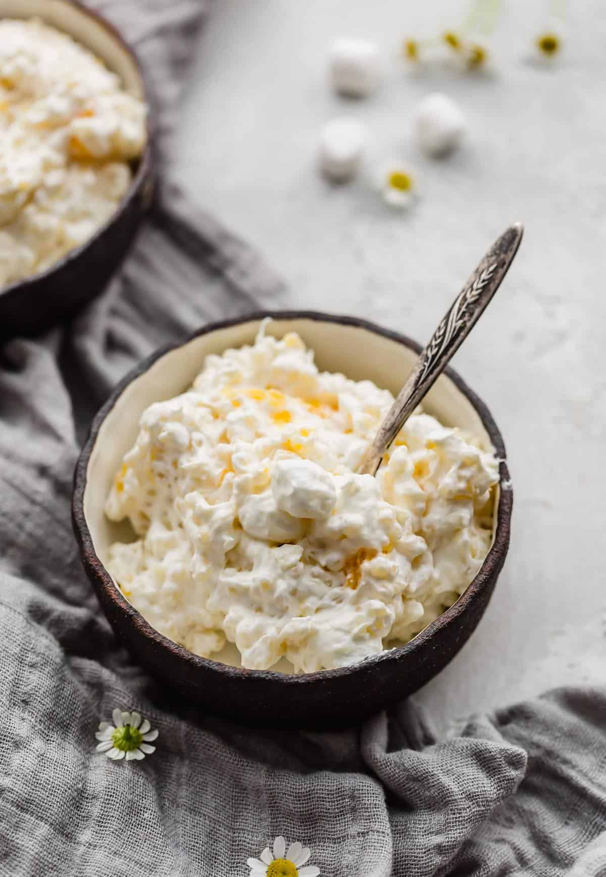 A black bowl filled with Acini di Pepe Pasta Salad, or frog eye salad, loaded with mandarin oranges, marshmallows, and cool whip.