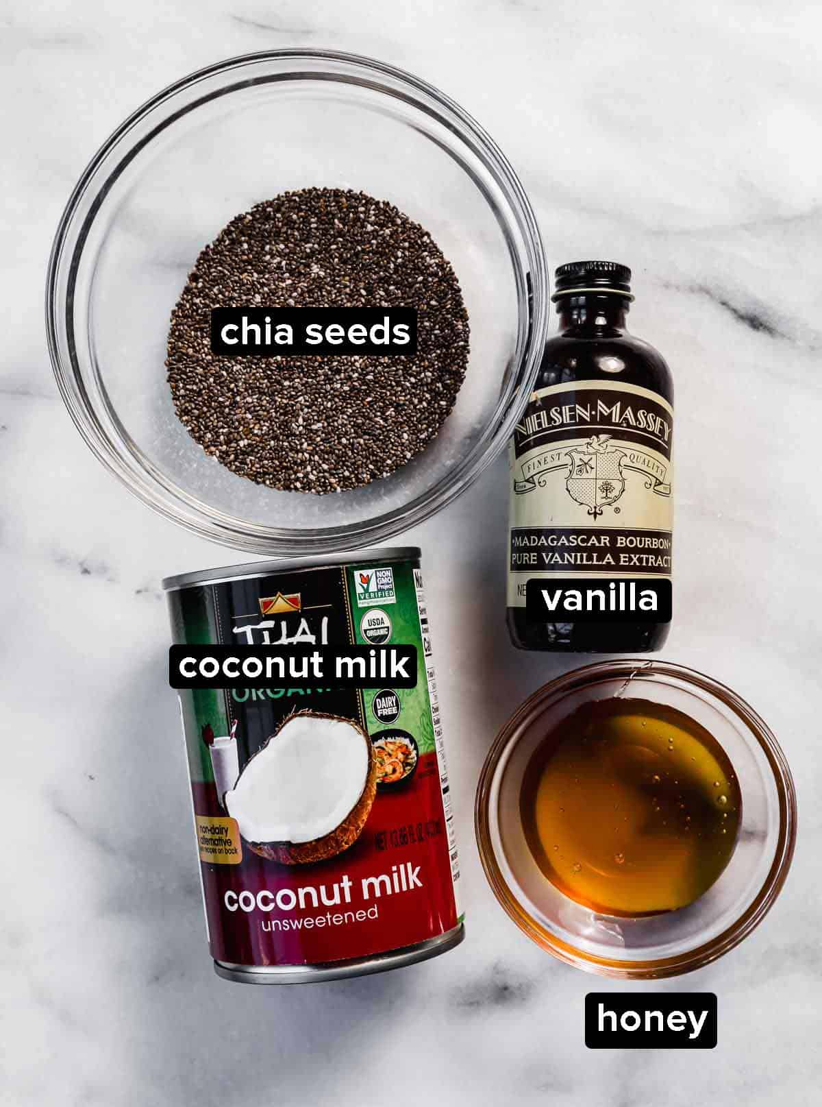 Coconut chia pudding ingredients on a white marble background: chia seeds, vanilla, coconut milk, and honey.