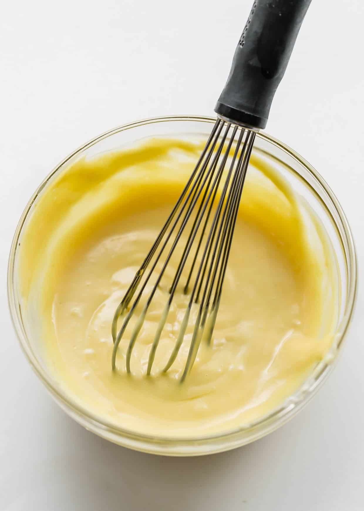Homemade honey mustard in a glass bowl on a white background.
